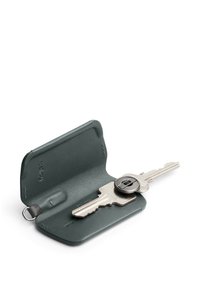 Porte-clés en cuir vert, présentant une texture lisse, une forme arrondie et une intégration visible de la clé avec un accent circulaire en métal.