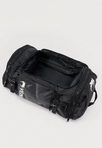 Mustast duffelkotist kott lukuga, mille sees on tekstuuriga vooder ja ühel küljel graafiline disain. Varustatud plastklambritega sulgude ja käepidemetega.