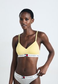 Gul seamless bralette med tynne stropper og V-hals. Inkluderer et hvitt belte med røde og blå logoer. Grå matchende undertøy med logobånd.