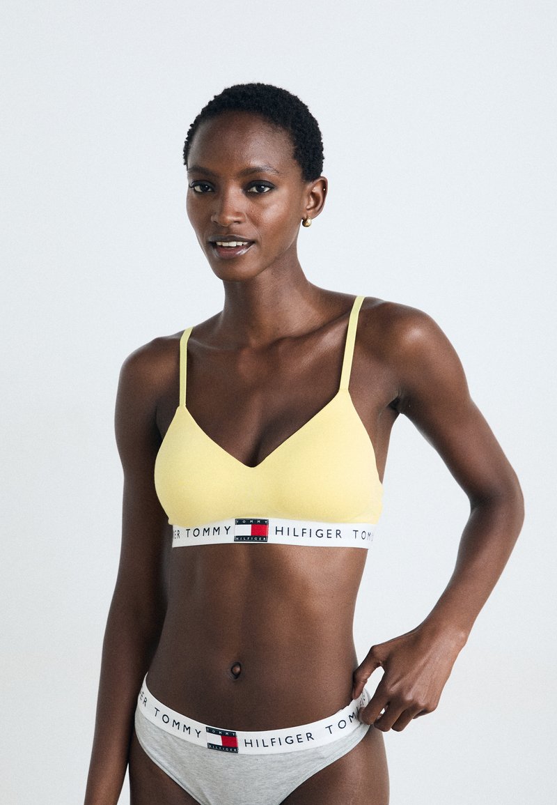 Gul seamless bralette med tynne stropper og V-hals. Inkluderer et hvitt belte med røde og blå logoer. Grå matchende undertøy med logobånd.