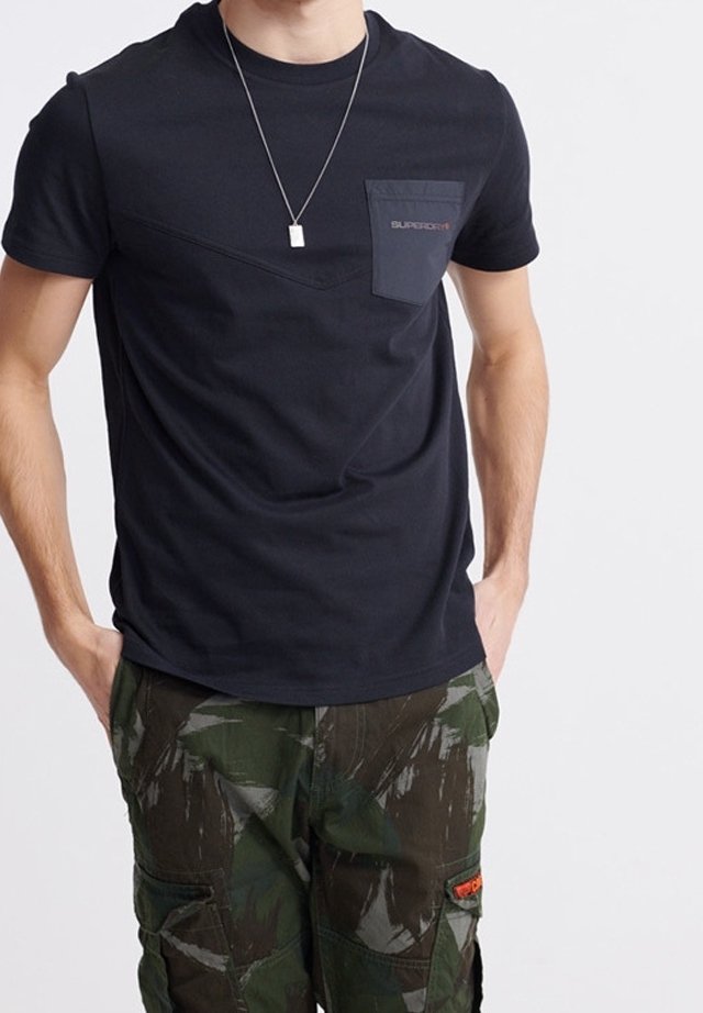 Sort kortærmet t-shirt med en brystlomme og et kontrasterende trekantet panel; parret med grønne camo cargo-bukser med sidelommer.