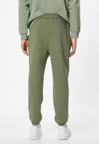 Joggers ajustados de color verde oliva, hechos de una tela suave, con cinturilla y puños elásticos, que incluyen bolsillos laterales y una textura suave.