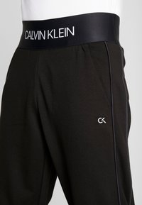 Zwarte jogger broek gemaakt van zachte stof, met een brede elastische tailleband met het label "CALVIN KLEIN," en een subtiele logo op het been.