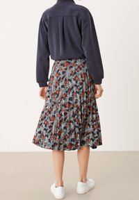 Jupe midi plissée à imprimé floral sombre, mettant en avant des nuances de rouge, de vert et de marine. Associée à un haut marine et des baskets blanches.