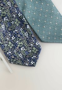 Două cravate: una bleumarin cu un model floral în verde și alb, și una texturată de un albastru deschis cu puncte mici bej. Ambele sunt cravate din material textil.