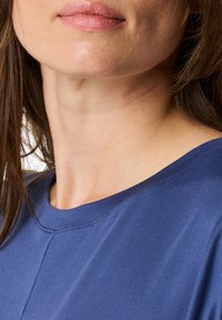 Niebieski top z okrągłym dekoltem wykonany z gładkiego materiału, charakteryzujący się delikatnym połyskiem oraz starannymi szwami w okolicy dekoltu i ramion, podkreślający luźny krój.