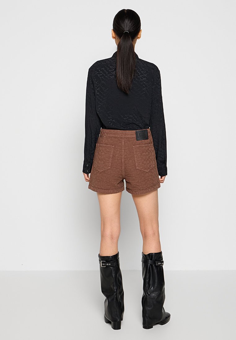 Schwarzes langärmliges Hemd, braune strukturierte Shorts mit Fronttaschen und knielangen schwarzen Lederstiefeln. Glattes Material mit leichtem Glanz.