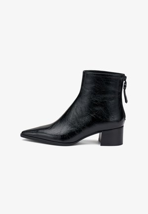 Bottines en cuir noir brillant avec un bout pointu, un talon bloc et une tirette à l'arrière sur fond blanc.