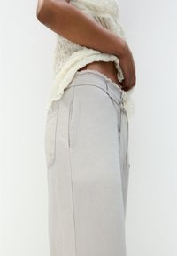 Lys grå linnedragt med vidde, sidelommer, afslappet pasform og snor i taljen, parret med en struktureret off-white top.