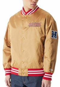 Giacca bomber in satin dorato con colletto e polsini a righe rosse e bianche. "49ERS" ricamato in rosso sul davanti; logo NFL sulla manica.