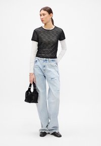Camiseta negra de rayas transparentes superpuesta sobre una camiseta blanca de manga larga, combinada con unos pantalones vaqueros de pierna ancha en un azul claro desgastados y un pequeño bolso negro.