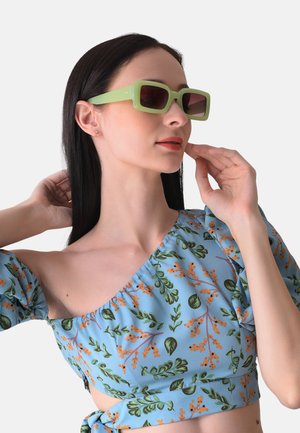 Grüne rechteckige Sonnenbrille mit getönten Gläsern, getragen mit einem hellblauen Oberteil mit Blumenmuster, das orangefarbene und grüne botanische Designs aufweist.