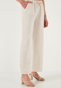 Beige linnen broek met een losse pasvorm en een elastische tailleband, voorzien van zijzakken en een rechte pijpdesign.