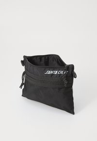 Zwarte tas met dubbele ritsen, waarvan de ene is voorzien van gaasstof en de andere van een gladde stof. De voorkant heeft het "SANTA CRUZ" logo in het wit.