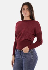 Maglione bordeaux con parte superiore testurizzata e scintillante e orlo a coste. Maniche lunghe e design aderente, abbinato a jeans blu.