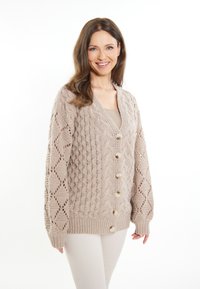 Cardigan lavorato a maglia di un beige chiaro, con motivi strutturati e chiusura frontale con bottoni. Maniche lunghe con dettagli a giorno.