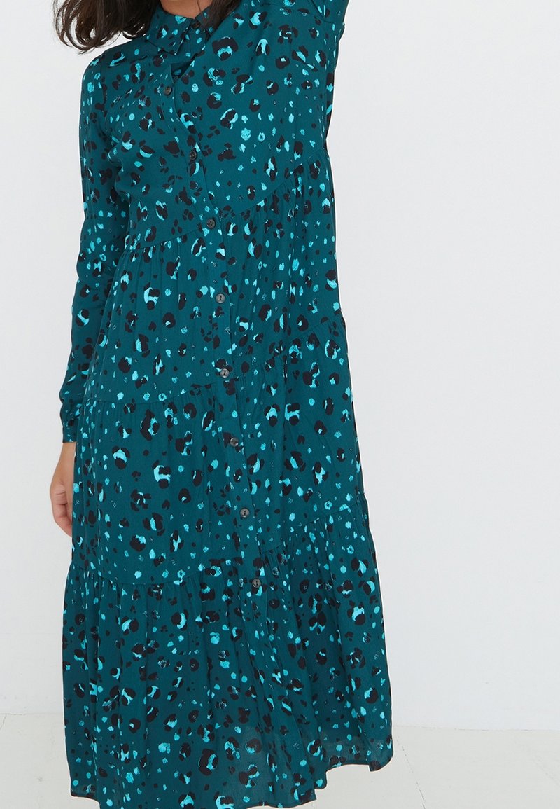 Abito verde acqua con design a strati e chiusura con bottoni, caratterizzato da una stampa leopardata bold in nero e blu su un tessuto leggero.