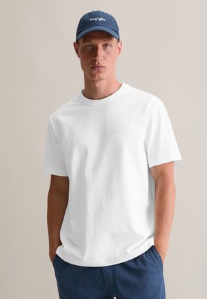 Witte katoenen t-shirt met een ronde halslijn, met een reliëflogo. Gecombineerd met marineblauwe shorts en een bijpassende pet met de tekst "Out of Office."