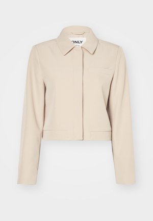 Kärbitud beež jakk kraega, pikkade varrukatega, ühe rinnataskuga ja siledas kangas. Minimalistlik disain, ilma nähtavate kinnitusteta.