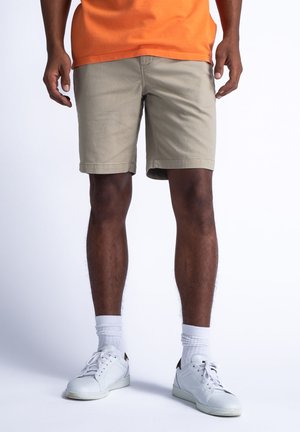 Khakifarbenen Shorts mit geradem Schnitt, aus einem Baumwollmischgewebe, kombiniert mit weißen Sneakers und knöchelhohen weißen Socken.