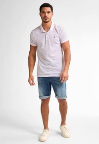 Pruhované polo tričko světle růžové barvy s oranžovými akcenty, nošené s ohrnutými džínovými šortkami a béžovými teniskami, představující neformální letní vzhled.