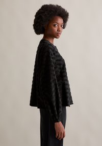 Schwarzes, strukturiertes Pulloveroberteil mit lässiger Passform, langen Ärmeln und Rundhalsausschnitt, das erhöhte horizontale Muster aufweist.