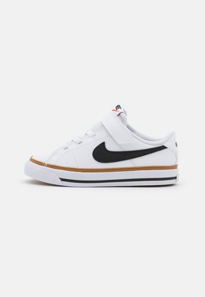 Biały sneaker Nike z czarnym logo Swoosh, brązową lamówką, paskiem na rzep i białą podeszwą z czarnymi paskami, przedstawiony z boku.