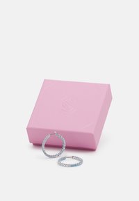 Orecchini a cerchio in argento con gemme blu incastonate in un design circolare, accanto a una scatola regalo rosa texturizzata.