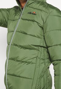 Zelená péřová bunda s prošívanými částmi, předním zipem a logem "ellesse" vytištěným na levé hrudi. Hladká, lesklá tkanina.