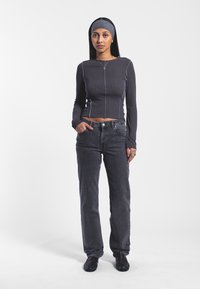 Maglia grigia a coste a maniche lunghe con cuciture a contrasto, abbinata a jeans scuri a vita alta. Scarpe nere completano il look casual.