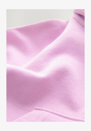 Tissu rose pâle avec une texture douce, présentant des plis et une apparence lisse, avec un détail de couture près du bas.