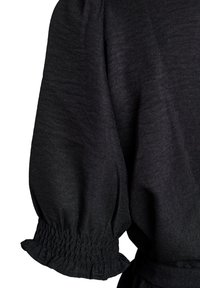 Zwarte stoffen mouw met elastische geplooide manchet en licht opgeblazen ontwerp op een kledingstuk tegen een witte achtergrond.