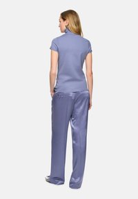 Helles lila, figurbetontes Polo mit hohem Kragen und kurzen Ärmeln, kombiniert mit lockeren, glänzenden, helllila Hosen mit seitlichen Taschen.