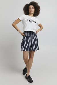 Hvid grafisk t-shirt med sort tekst, parret med en marineblå stribet nederdel med smocket talje; sorte sko fuldender outfittet.