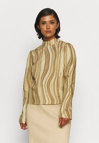 Blusa de mangas longas em bege com padrão de ondas castanho, apresentando um decote alto e ombros ligeiramente bufantes. Textura suave.