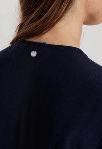 Granatowy top z okrągłym dekoltem, z tyłu z okrągłym, srebrnym guzikiem oraz gładkim, lekko teksturowanym materiałem.