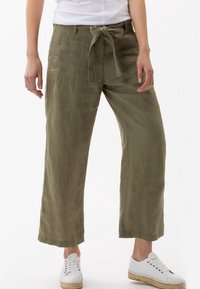 Khaki linned brede bukser med bundet talje, sidelommer og en glat tekstur, parret med hvide snørebåndssneakers.