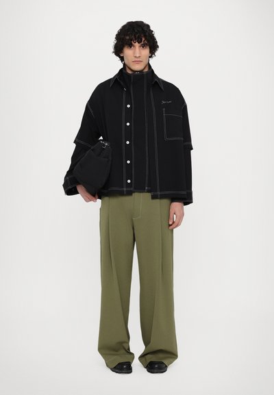 Black oversized shirt with white stitching details, black pants, and a black bag. The shirt features buttons and a chest pocket.