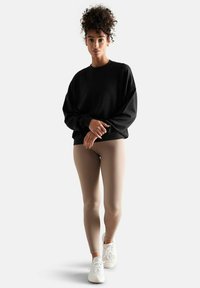 Sweatshirt noir à épaules tombantes, leggings beiges et baskets blanches, sur fond uni. Tissu doux, design décontracté.