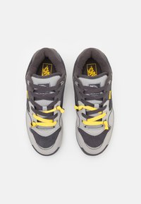 Gray and black sneakers with yellow laces and accents, featuring a textured suede and mesh upper, padded collar, and logo detail.
