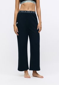 Zwarte wijde pantalons gemaakt van zacht materiaal, met een elastische tailleband met een merklogo. Geen patronen; gladde textuur.