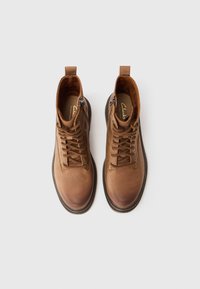 Une paire de bottines en cuir marron à lacets avec fermetures éclair sur les côtés, vue de dessus sur un fond blanc.
