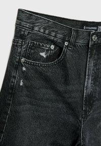 Jeans en denim noir avec un design déchiré, des coutures visibles et une fermeture éclair avec un bouton en métal. Légère décoloration sur l'ensemble.
