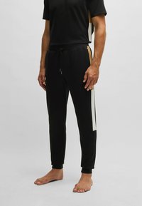 Black athletic pants with white side stripes, drawstring waistband, and fitted cuffs. Paired with a black short-sleeve top.
