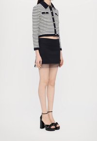 Striped cropped jacket in navy and white, button front, paired with a black mini skirt featuring a sheer trim, complemented by black platform sandals.