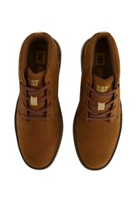Zapatos de ante marrón con puntera redonda, cuello acolchado y diseño con cordones. Presenta una pequeña etiqueta beige y un logotipo en la lengüeta. Suela de goma.