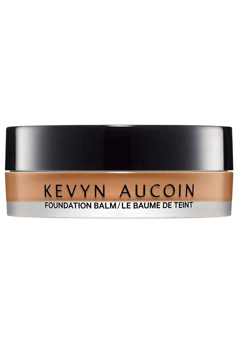 Baume de la fondation Kevyn Aucoin dans un conteneur rond avec un couvercle noir, produit crémeux beige visible, texte étiqueté sur le devant.