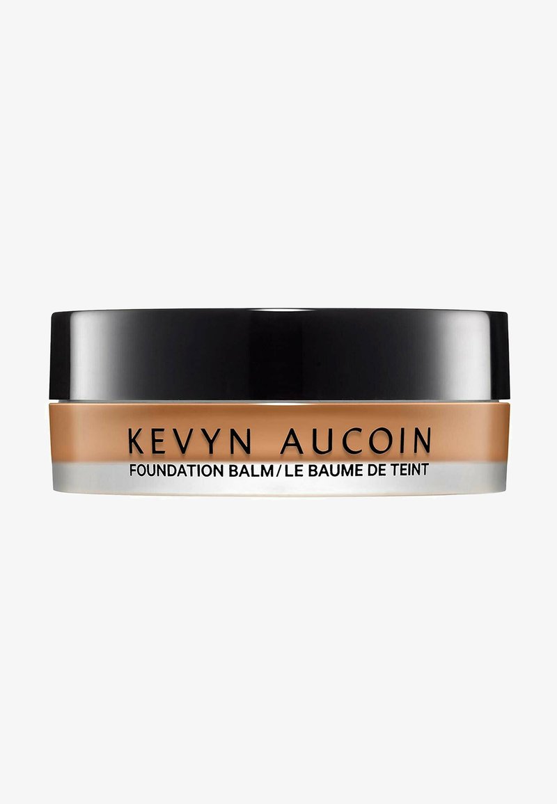 Baume de la fondation Kevyn Aucoin dans un conteneur rond avec un couvercle noir, produit crémeux beige visible, texte étiqueté sur le devant.