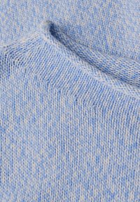 Gros plan sur un tissu tricoté bleu clair et blanc montrant la texture détaillée des mailles et le bord de couture plié.