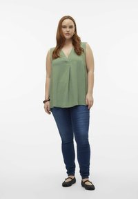Grön, ärmlös topp med V-ringning och plisserad design, kombinerad med medelblå, slim fit-jeans och svarta lägenheter. Slät tygtextur.